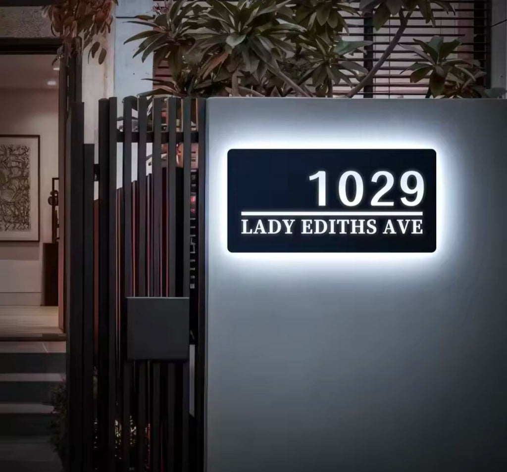 Modern rectangular custom LED house address sign glowing white with number and street name on wall at night