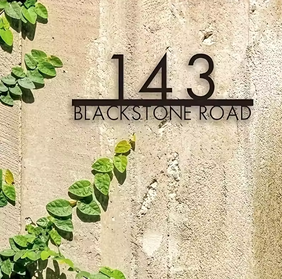 metal floating House number '143' on a stone wall with greenery