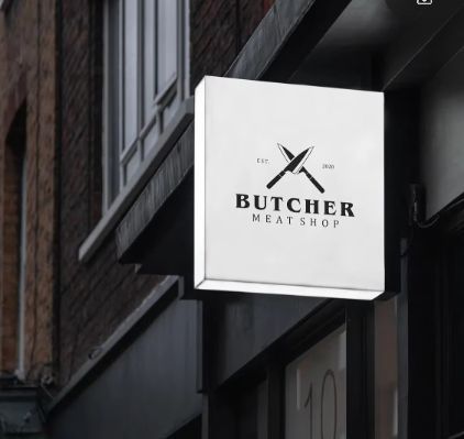 Square acrylic LED lightbox sign with butcher shop logo mounted on a building exterior at dusk