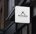 Square acrylic LED lightbox sign with butcher shop logo mounted on a building exterior at dusk