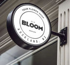 Round double-sided business signage lightbox mounted on a building exterior for a flower shop.