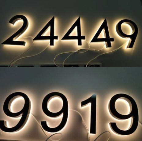 Matte black custom metal LED house numbers glowing softly with visible wiring against a dark background.