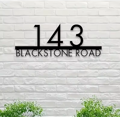 House number '143 Blackstone Road' on a white brick wall with green plants at the bottom.