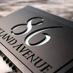 Close-up of a modern custom acrylic house sign with laser-etched numbers and street name on black panel.
