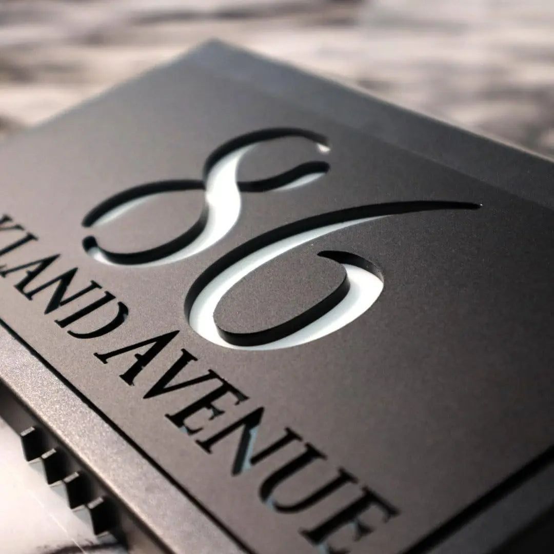 Close-up of a modern custom acrylic house sign with laser-etched numbers and street name on black panel.