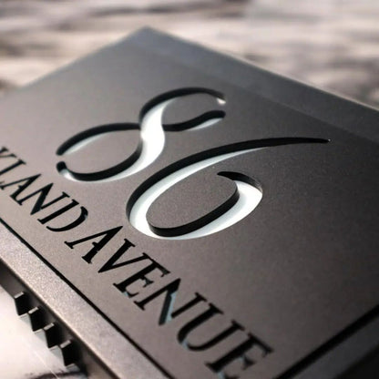 Close-up of a modern custom acrylic house sign with laser-etched numbers and street name on black panel.
