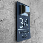 Rectangular custom acrylic house number sign with mirrored cutout lettering and a modern light fixture above.
