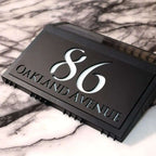 Modern black solar-powered acrylic house number sign with backlit white engraving for 86 Oakland Avenue.