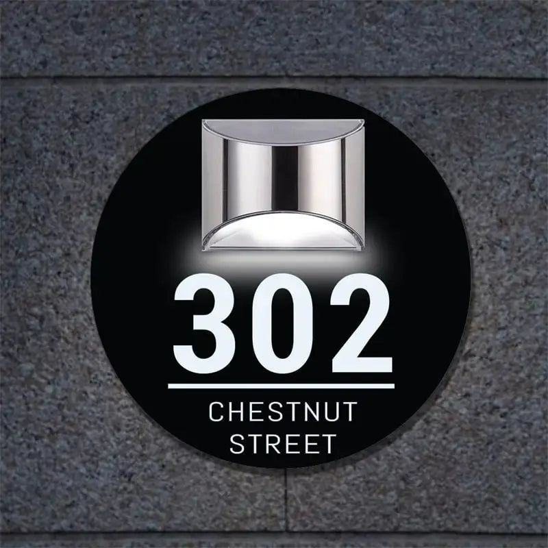 Circular solar-powered acrylic house sign with custom laser-etched address mounted on dark textured wall